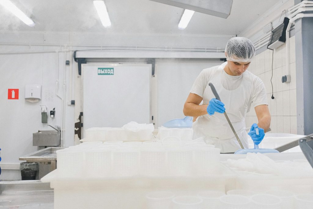Un homme en tenue stérile travaille dans une fromagerie, veillant au respect des normes d'hygiène.